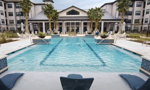 Relax and unwind poolside resort style pool with seating palm trees and a building behind it